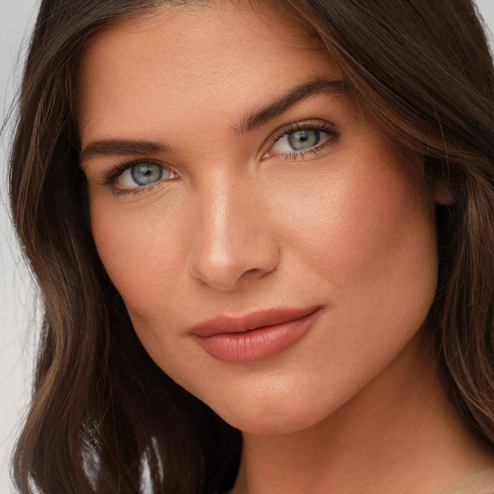 Close-up of a woman with brown hair and blue eyes, wearing Moonglow makeup.
