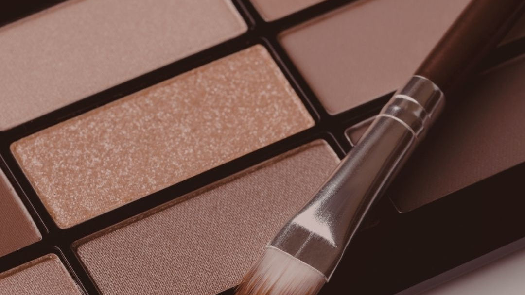 Makeup palette with brown shades and a brush on a neutral background