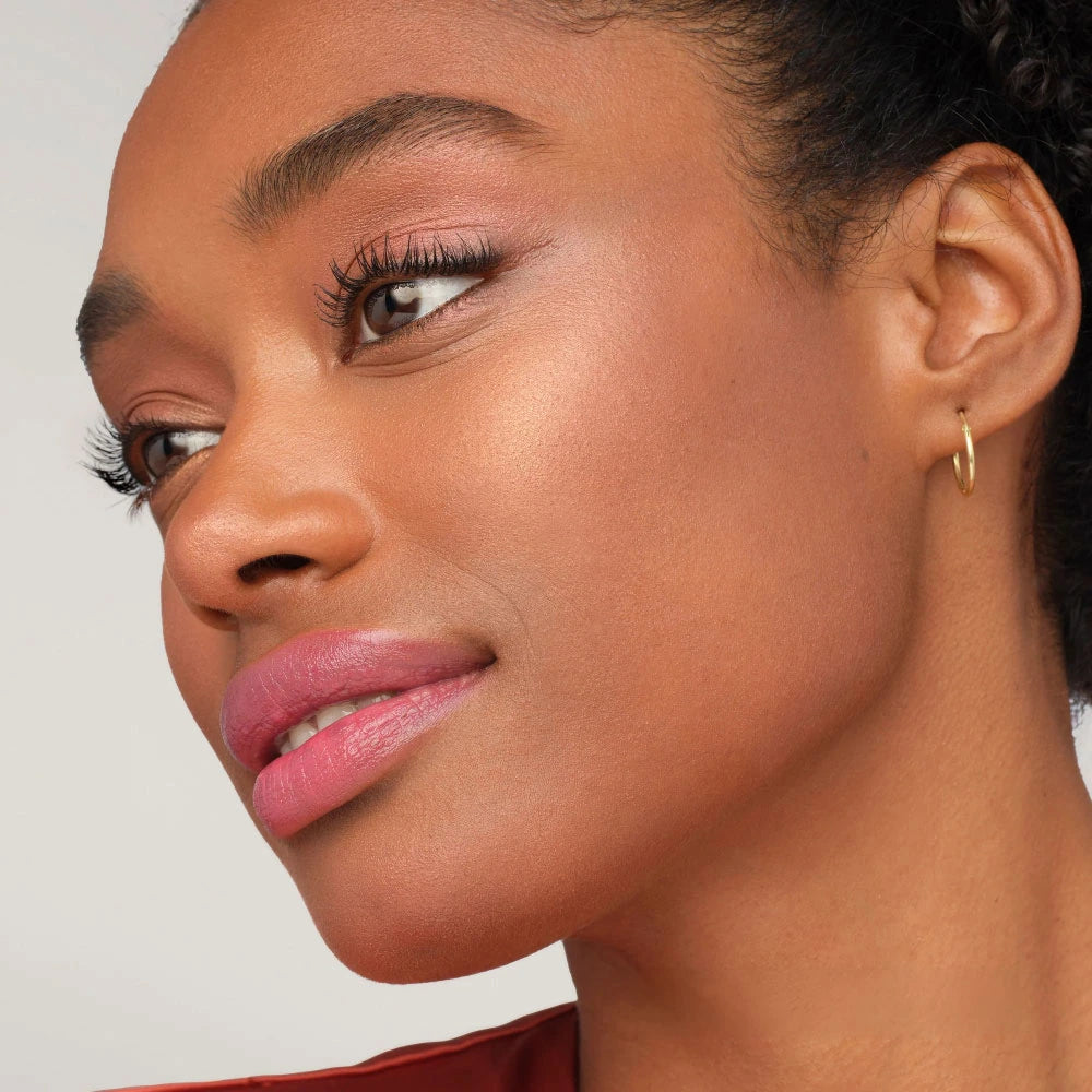 Close-up of a woman's face wearing pink lipstick and gold earrings with a neutral background.